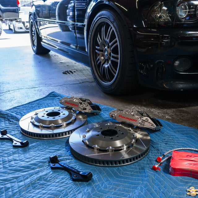 Paragon brake rotors, nickel-plated calipers and mounting brackets laid out beside a BMW E46 M3